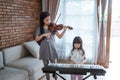 Little girl plays a musical instrument piano with her sister playing the violin together Royalty Free Stock Photo