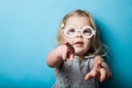 A little girl points with fingers and hands. Toy fashion glasses