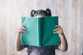 Little girl with ponytail reading a book while covering her face Royalty Free Stock Photo