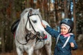 Little girl portrait, stands next to a white pony close-up on the background of nature. Jockey, epodrome, horseback riding Royalty Free Stock Photo