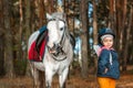Little girl portrait, stands next to a white pony close-up on the background of nature. Jockey, epodrome, horseback riding Royalty Free Stock Photo