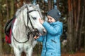 Little girl portrait, stands next to a white pony close-up on the background of nature. Jockey, epodrome, horseback riding Royalty Free Stock Photo