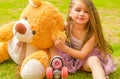 Little girl preschool sitting on backyard next to her teddy bear, wearing her roller skates and crossing her legs, in a Royalty Free Stock Photo