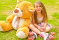 Little girl preschool sitting on backyard next to her teddy bear, wearing her roller skates and crossing her legs, in a Royalty Free Stock Photo