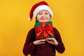 Little girl with a present. A child holds a gift under his head in a Christmas hat on a yellow background Royalty Free Stock Photo