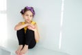 A little girl pretends to be an adult woman or her mommy with curlers in her hair sitting near a white wall. The concept