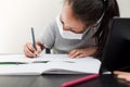 Little girl in a protective face mask does homework for school during quarantine. Distance learning online education during the Royalty Free Stock Photo