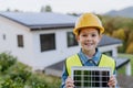 Little girl with protective helmet and reflective vest holding photovoltaics solar panel. Alternative energy, saving