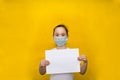 Little girl in a protective mask holds a blank sheet of paper on a yellow background. Protection against coronavirus Royalty Free Stock Photo