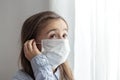 Little girl in a protective medical mask stands near the window close up Royalty Free Stock Photo