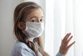 Little girl in a protective medical mask stands near the window close up Royalty Free Stock Photo