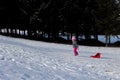 A little girl pulls a bobsled by the string up a snowy steep hill Royalty Free Stock Photo