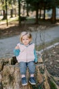 Little girl pursed her lips while sitting on a stump covered with ivy in the park Royalty Free Stock Photo