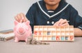 Little girl  putting coin into piggy bank for saving with pile of coins on table Royalty Free Stock Photo