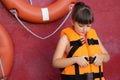 Little girl putting on orange life vest near red wall with safety rings Royalty Free Stock Photo