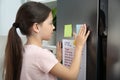 Little girl putting sticky note near to do list in kitchen