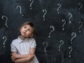 Little girl with question marks on blackboard. Concept for confusion, brainstorming and choice. Royalty Free Stock Photo