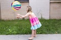 Little girl in rainbow coloured summer dress throwing multicolored beach ball