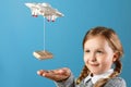 A little girl reaches out to a packaged box tied to a copter. The concept of delivery, transportation, service. Blue background