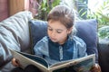Little girl is reading a book in the living room on the couch Royalty Free Stock Photo