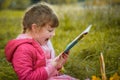 Little girl is reading a book in the park. A baby with a book is sitting on the grass. A child in a pink jacket screams gaily Royalty Free Stock Photo