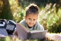 A little girl reading a book while relaxing in a park or garden. Mixed race child learning and getting an education Royalty Free Stock Photo