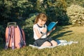 Little girl reading a book with a school backpack sitting on the grass in the park Royalty Free Stock Photo