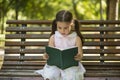 Little girl reading a book sitting on a bench in the garden Royalty Free Stock Photo