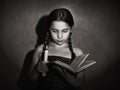 Little girl reading book and studying in candle light in dark room Royalty Free Stock Photo