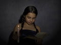 Little girl reading book and studying in candle light in dark room