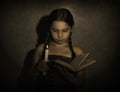 Little girl reading book and studying in candle light in dark room Royalty Free Stock Photo