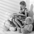 Little girl is reading a book to a teddy bear. Royalty Free Stock Photo