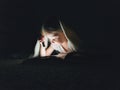 little girl is reading a book under a blanket with a flashlight in a dark room at night Royalty Free Stock Photo