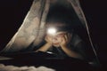 little girl is reading a book under a blanket with a flashlight in a dark room at night Royalty Free Stock Photo