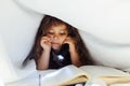 little girl reading a book under a blanket with a flashlight Royalty Free Stock Photo