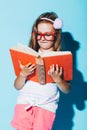 Little girl reading a book, wearing funny red glasses. Royalty Free Stock Photo