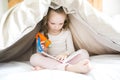 Little girl reading fairy tales book under the covers at the evening with lantern. Royalty Free Stock Photo