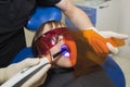 The little girl is receiving medical treatment of the stomatologist, doing procedure with dental curing UV light in clinic