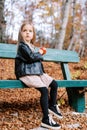 Little girl with a red apple in her hands sits on a wooden bench in the autumn forest and looks away Royalty Free Stock Photo