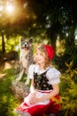 A little girl in a red cap and akita like a gray wolf, is friends sitting on the edge of the forest