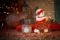 little girl in red dress against background of Christmas tree holds Christmas garland in her hands. baby 6 month old celebrates