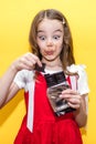 A little girl in a red dress holds a bar of chocolate in her hands on a yellow background Royalty Free Stock Photo