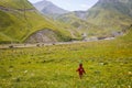 A little girl in a red dress and a knitted cap-strawberry runs on a green field in the mountains.