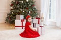 Little girl in red dress laughs and enjoys gift. Little girl opening magical christmas present at home. child holds christmas pres Royalty Free Stock Photo