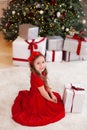 Little girl in red dress laughs and enjoys gift. Little girl opening magical christmas present at home. child holds christmas pres Royalty Free Stock Photo