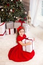 Little girl in red dress laughs and enjoys gift. Little girl opening magical christmas present at home. child holds christmas pres Royalty Free Stock Photo