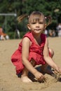 Little girl in a red dress plays with sand on the beach Royalty Free Stock Photo