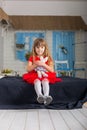 Little girl in a red dress sitting on the bed. Royalty Free Stock Photo