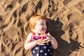 A little girl with red hair in a bathing suit is lying on the sand near the shore. Summer Royalty Free Stock Photo