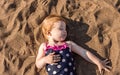 A little girl with red hair in a bathing suit is lying on the sand near the shore. Summer Royalty Free Stock Photo